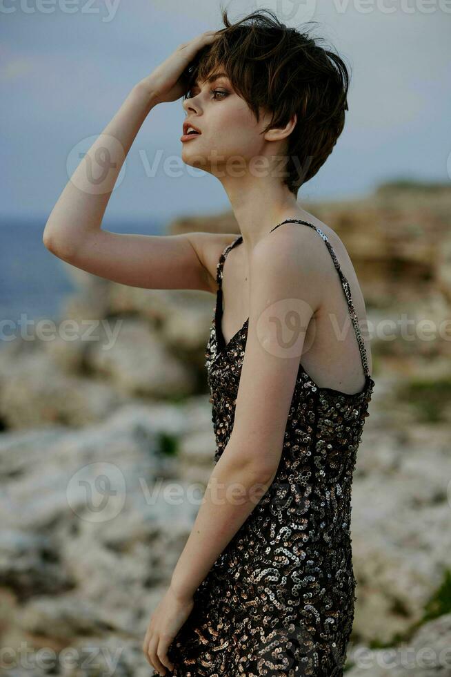 corto dai capelli donna nel brillante vestito in posa vicino rocce foto