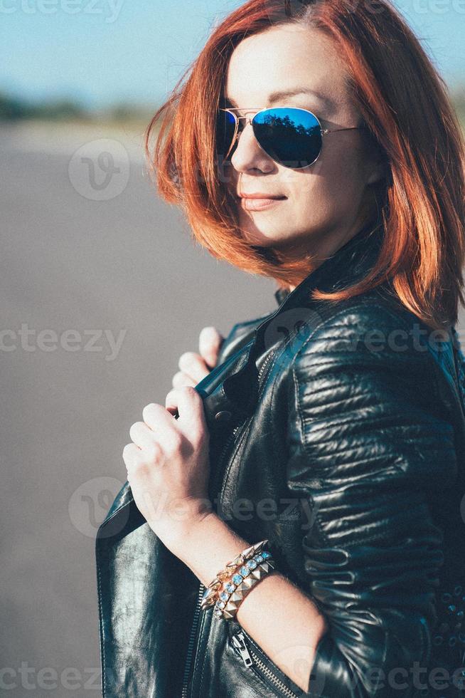 ragazza dai capelli rossi in una giacca nera e occhiali blu foto