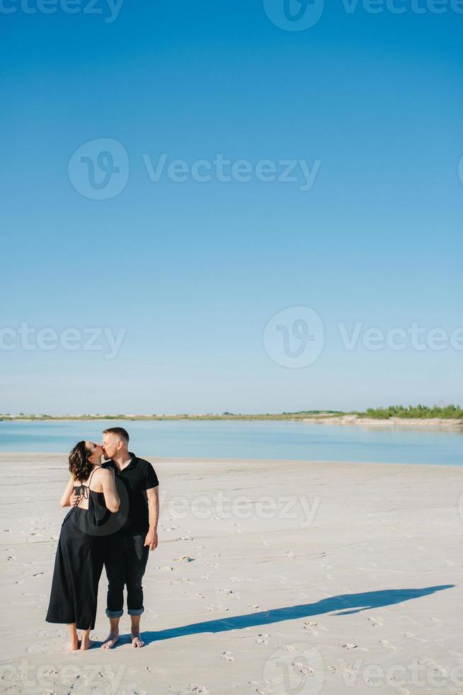 giovane coppia un ragazzo con una ragazza in abiti neri stanno camminando sulla sabbia bianca foto