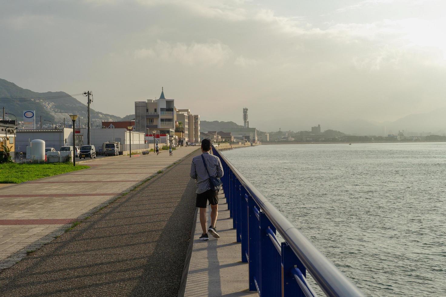 indietro ritratto di uomo che cammina lungo la diga in riva al mare nella giornata di sole foto
