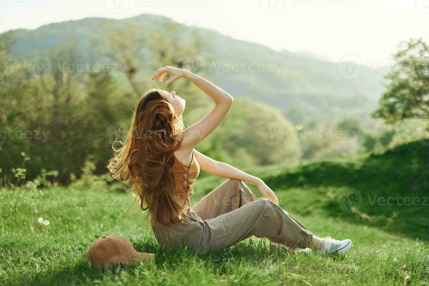 giovane donna con lungo rosso capelli rilassante nel abbigliamento sportivo su il erba nel un' natura parco, volante capelli, il concetto di un' salutare stile di vita e preoccupazione per il ambiente e ecologia foto