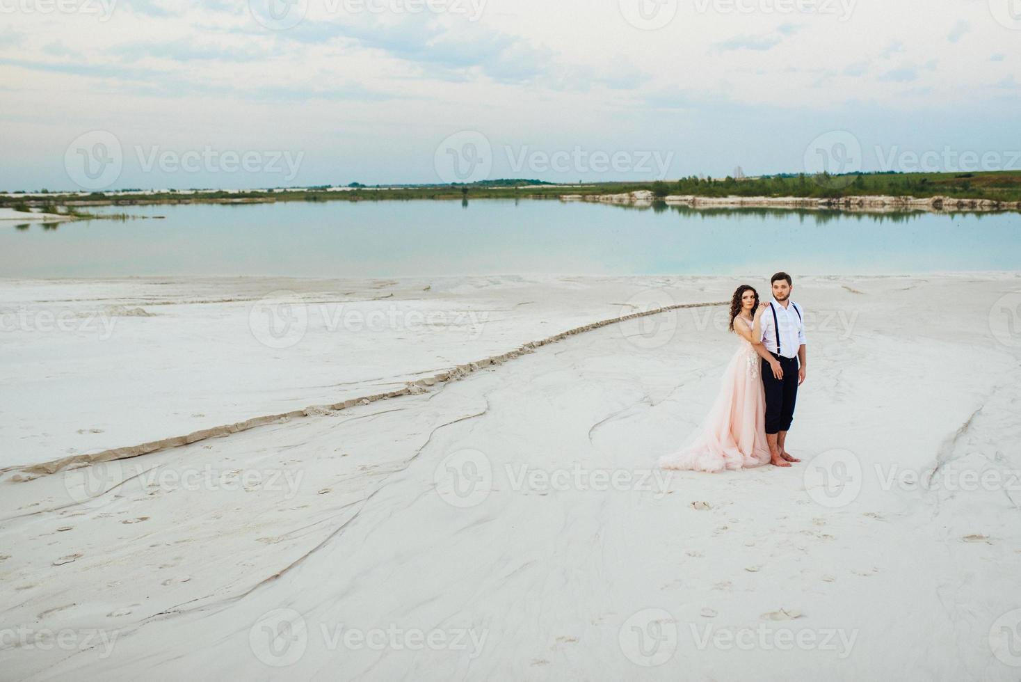 giovane coppia un ragazzo in calzoni neri e una ragazza in un vestito rosa stanno camminando lungo la sabbia bianca foto