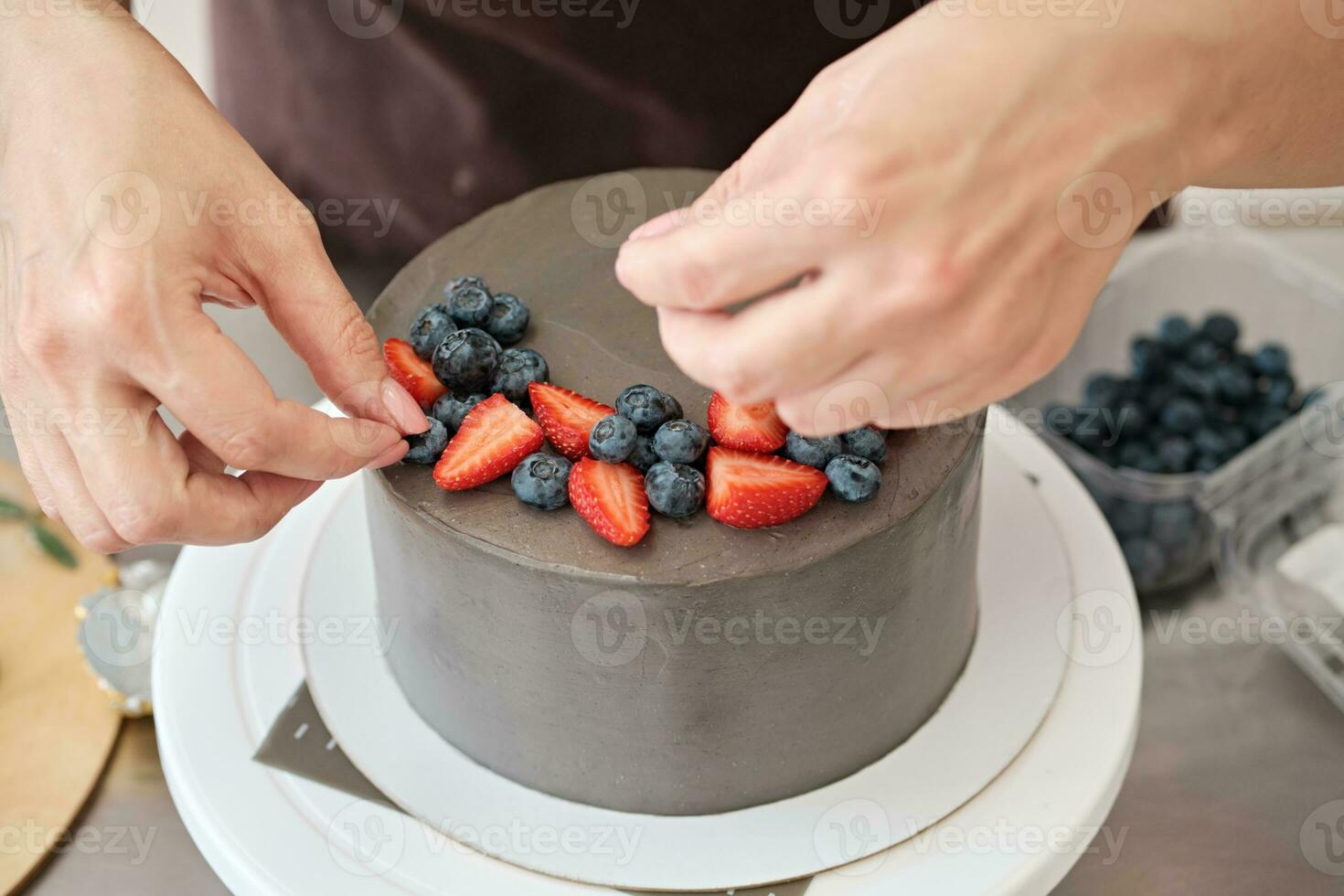 donna Pasticcino capocuoco decora grigio torta con frutti di bosco, avvicinamento. torta fabbricazione processi, selettivo messa a fuoco foto