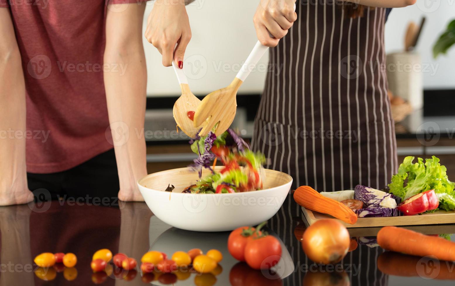 una giovane coppia asiatica sta mangiando insieme e sorridendo felicemente mentre cucina la loro insalata in cucina. foto