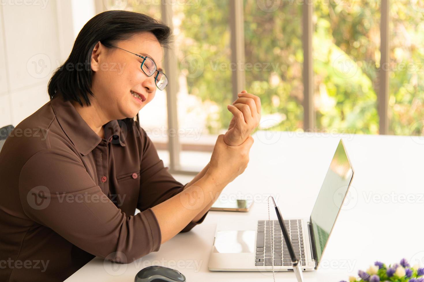 donna asiatica di affari che tiene il suo dolore al polso dal lavoro e dall'utilizzo del computer. sindrome dell'ufficio foto