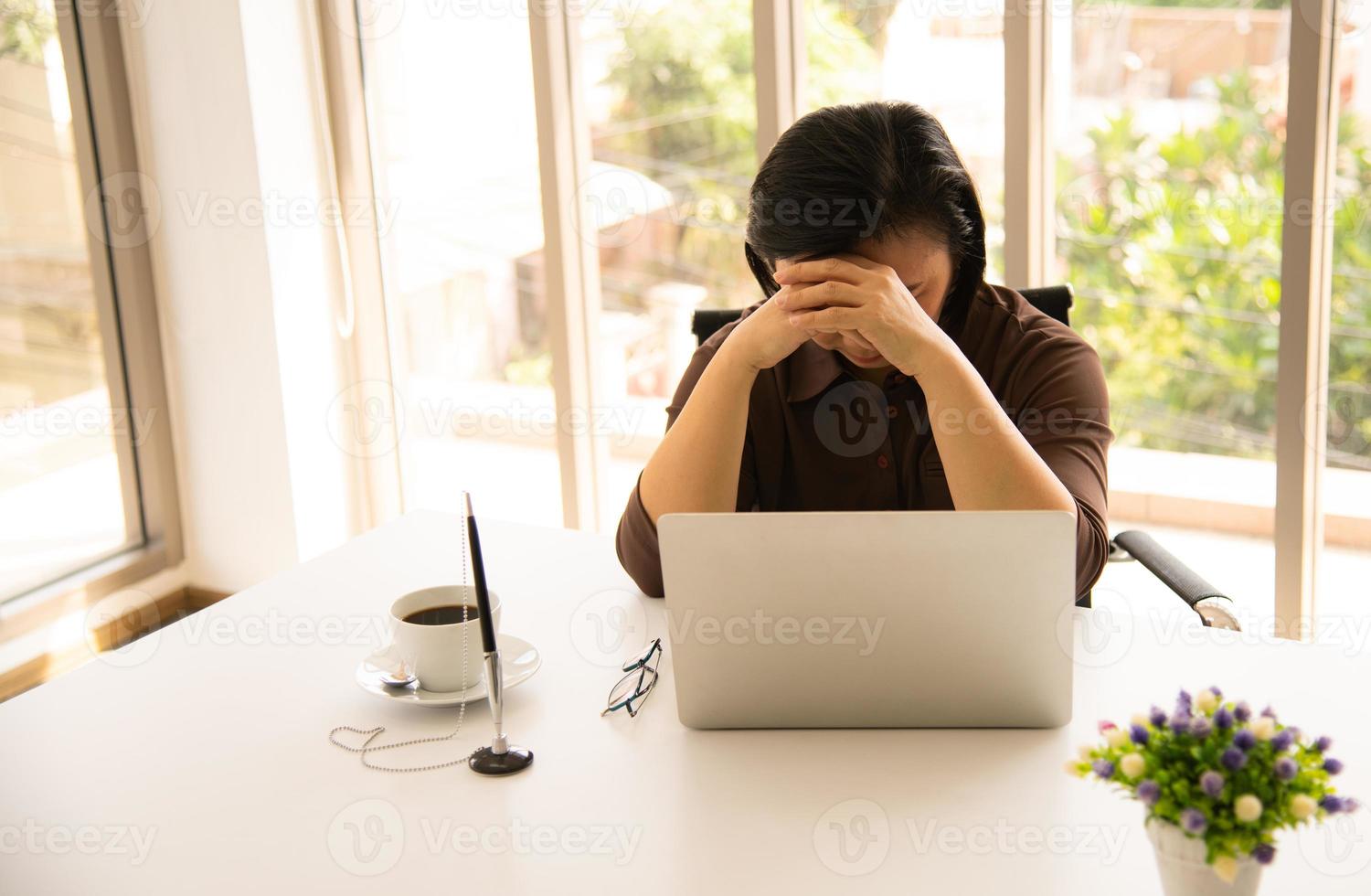 donna asiatica senior utilizzando un telefono cellulare e un computer portatile sullo sfondo naturale del soggiorno con la tecnologia moderna foto