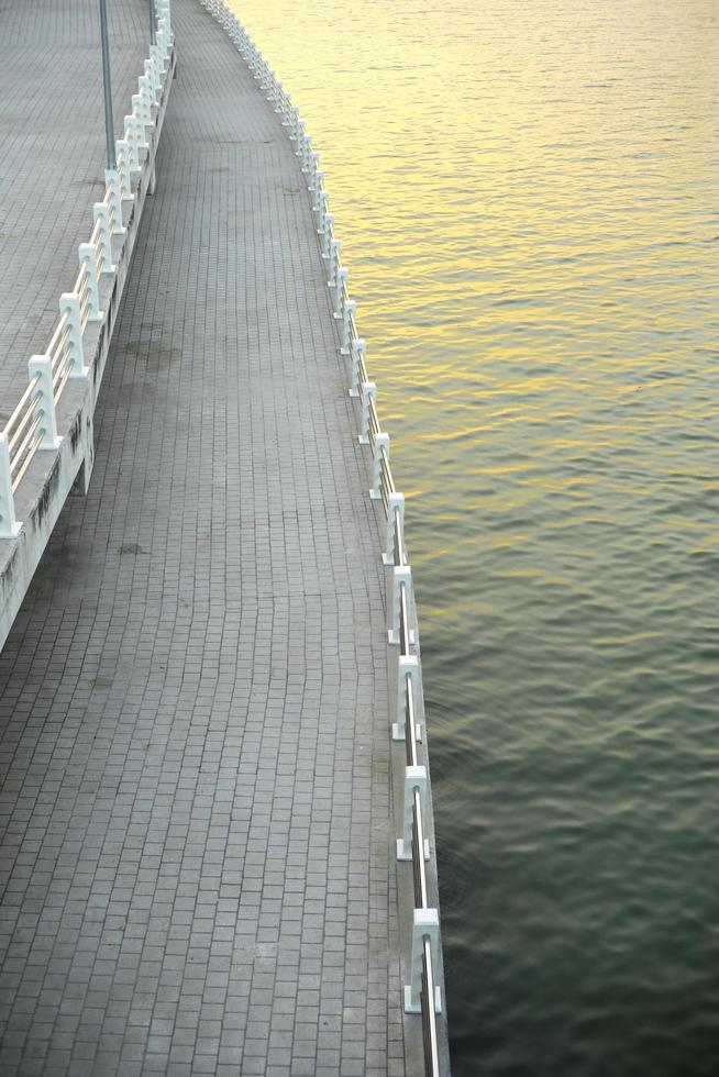 passerella in cemento vuoto lungo la riva di un fiume con la riflessione della luce dal sole foto