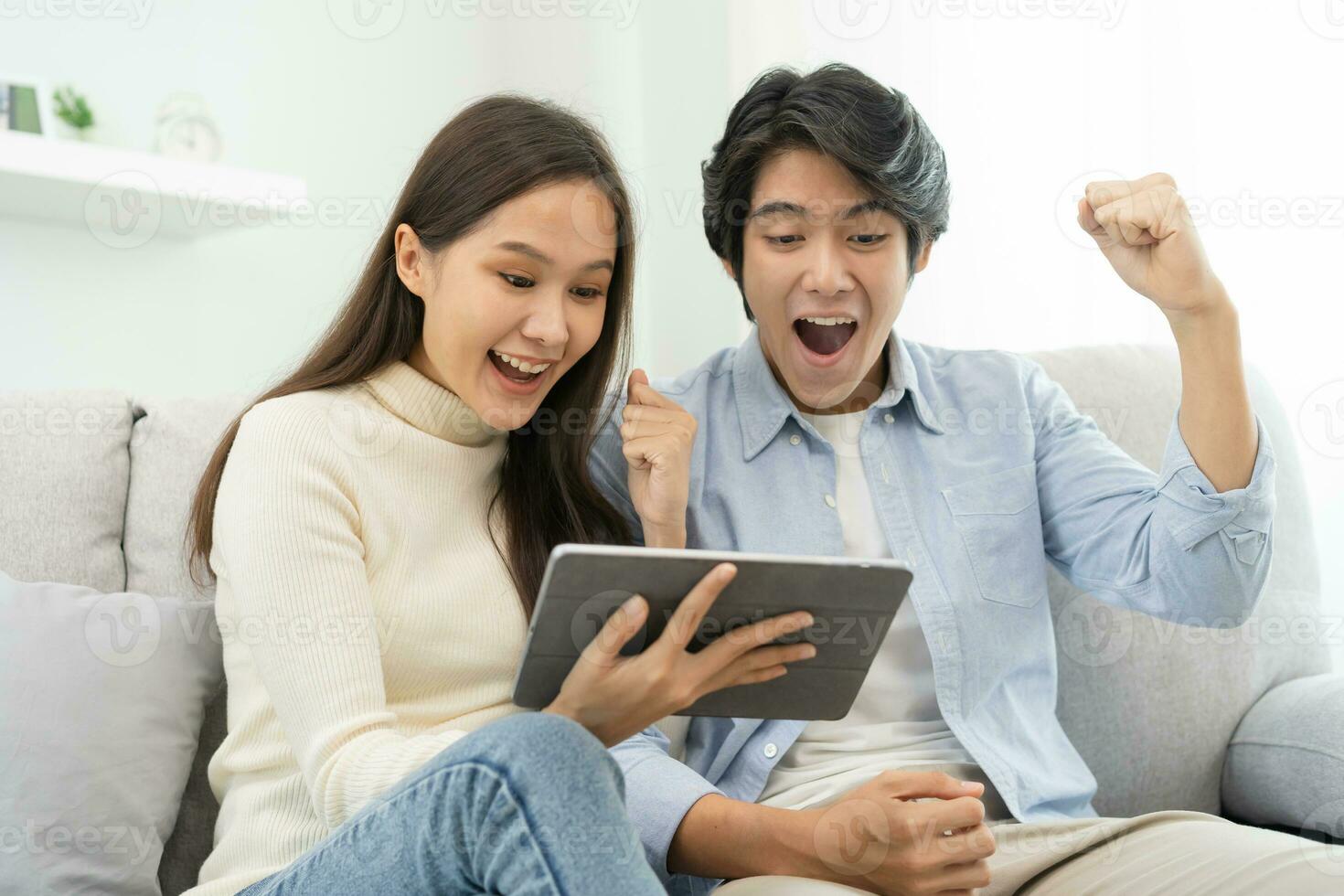 contento emozionato, sorridente asiatico giovane coppia amore utilizzando tavoletta pc, grande affare o attività commerciale successo, ricevuto o ottenere denaro contante Indietro, imposta rimborso, bene notizia di posta mentre seduta su divano, divano a casa. foto