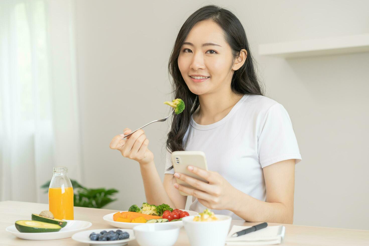 dieta, asiatico giovane donna mangiare, Tenere forchetta a broccoli, dieta Piano nutrizione con fresco verdure insalata, godere pasto mentre utilizzando smartphone. dietologo di sano, nutrizione di peso perdita. foto