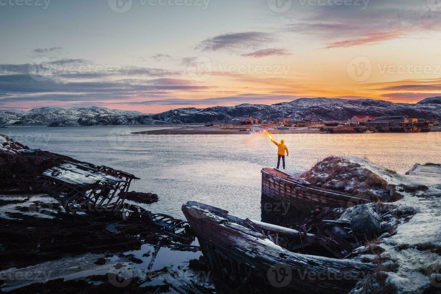 un' giallo figura con un' luce del fuoco. cimitero di navi, inverno tramonto Visualizza nel un vecchio pesca villaggio su il riva di il barents mare, il Kola penisola, teriberka foto