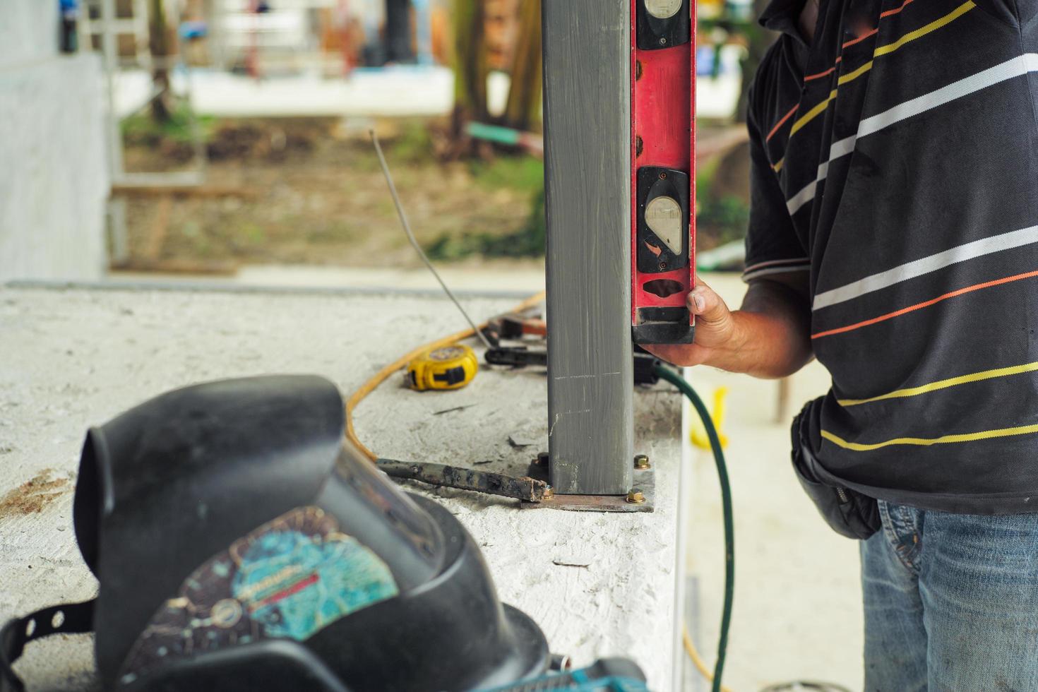 Il lavoratore misura il livello della perpendicolare durante l'installazione del palo d'acciaio in cantiere dal righello di livellamento foto