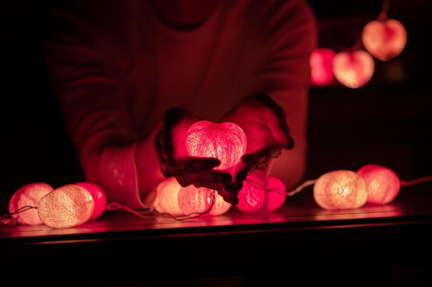 l'uomo tiene la lampada a led a forma di cuore nelle sue mani in una stanza buia foto