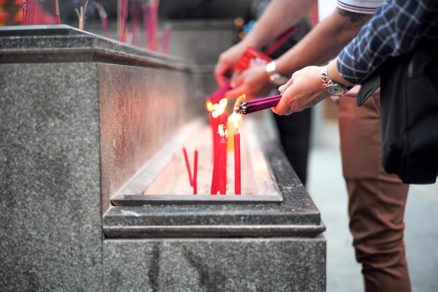 mani del primo piano che tengono il fascio di incensi per l'illuminazione con le candele nel vassoio della sabbia foto