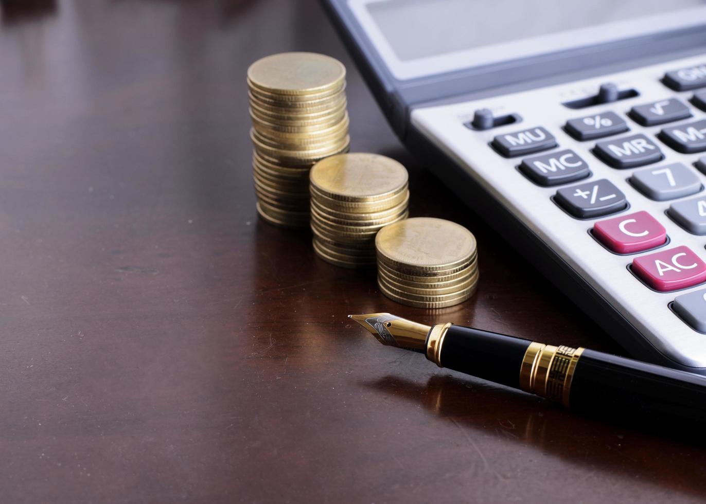 pila di monete e penna stilografica e denaro e calcolatrice per il concetto di finanza foto