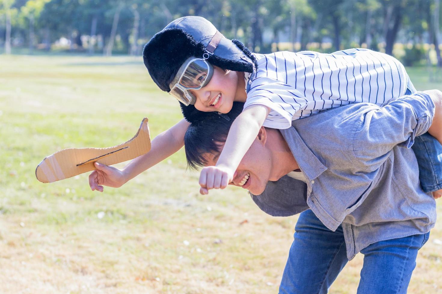 padre e figlio che giocano a aeroplani di carta nel parco. il figlio è sulla schiena di suo padre. foto