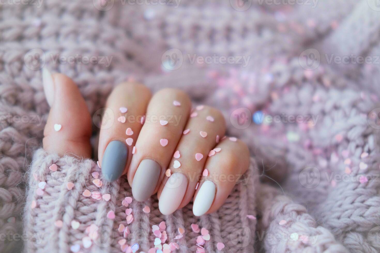 Da donna mani con un' bellissimo Opaco ovale manicure nel un' caldo viola a maglia maglione e cuore sagomato paillettes. inverno tendenza, polacco beige Chiodi con gel polacco, Gommalacca. copia spazio. foto