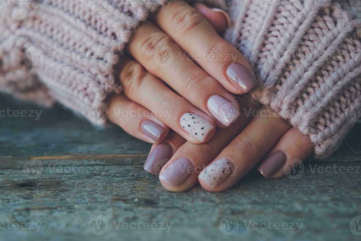 donne è mani con un' bellissimo manicure, nel un' a maglia maglione su un' di legno sfondo in. autunno tendenza, polacco il beige e Quaglia uovo modello su il Chiodi con gel polacco, Gommalacca. copia spazio. foto