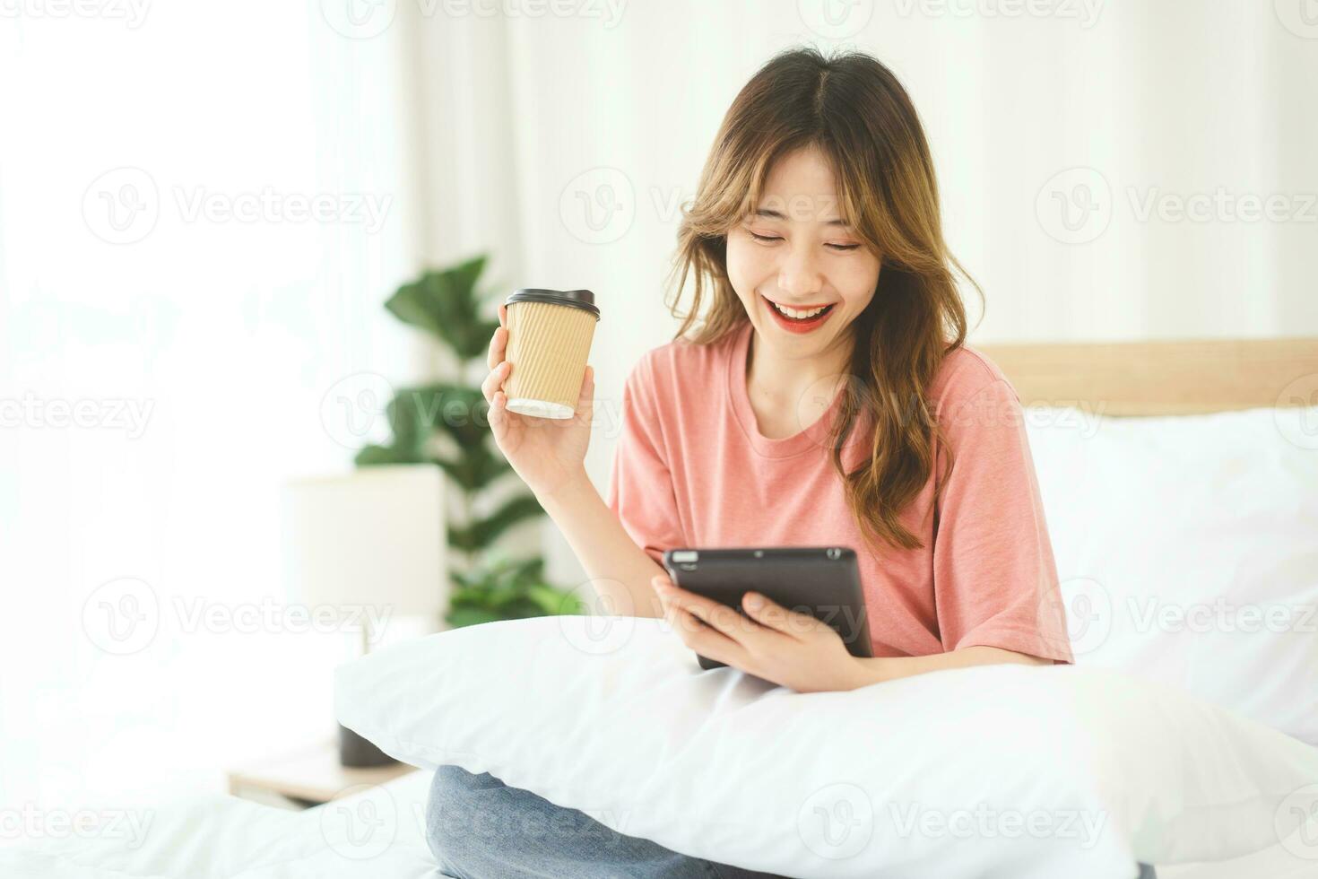 asiatico donna con caffè utilizzando digitale tavoletta per sociale Messaggio telemedicina e mentale Salute o shopping in linea su a Camera da letto mattina tempo foto