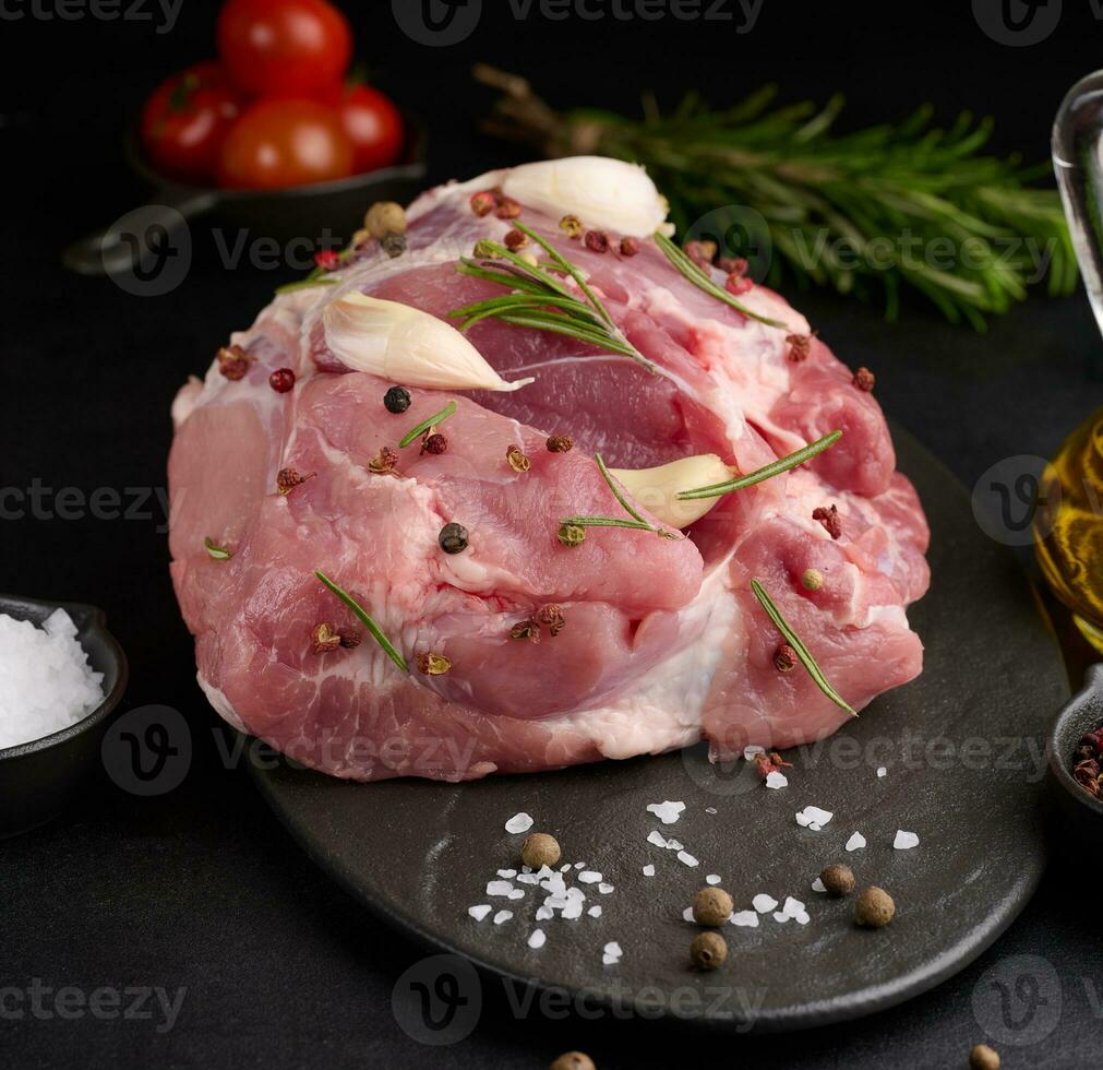 un' pezzo di Maiale prosciutto su un' nero tavola e spezie oliva olio, sale, rosmarino ramo e Pepe foto