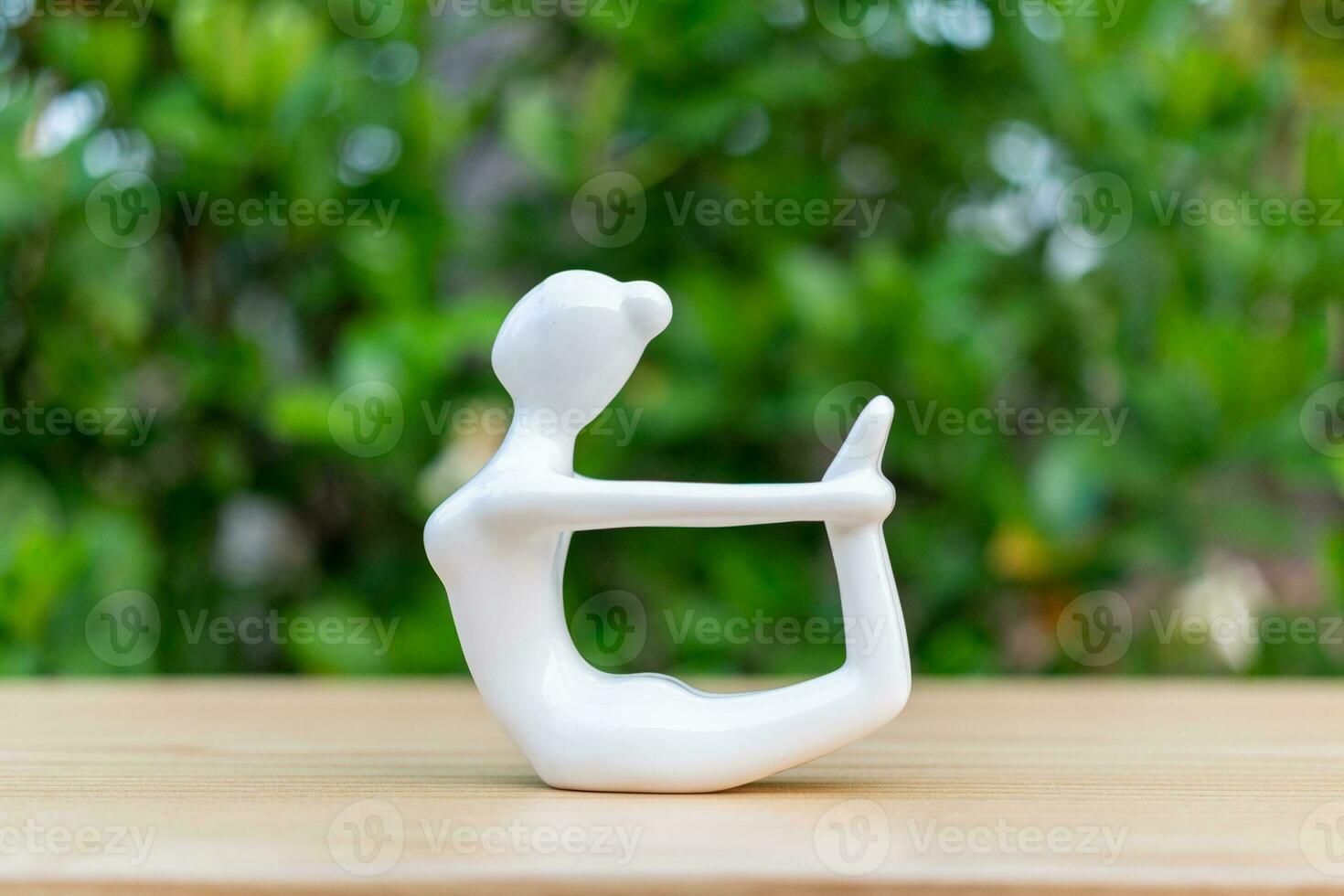 ceramica yoga figurina di donna fare yoga posa su di legno pavimento e verde foglia sfondo foto