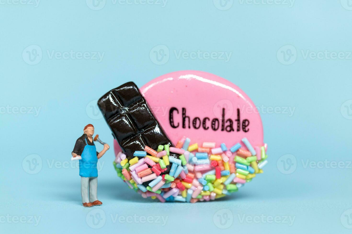 miniatura le persone, capocuoco con cioccolato biscotto su un' blu sfondo. mondo cioccolato giorno concetto foto