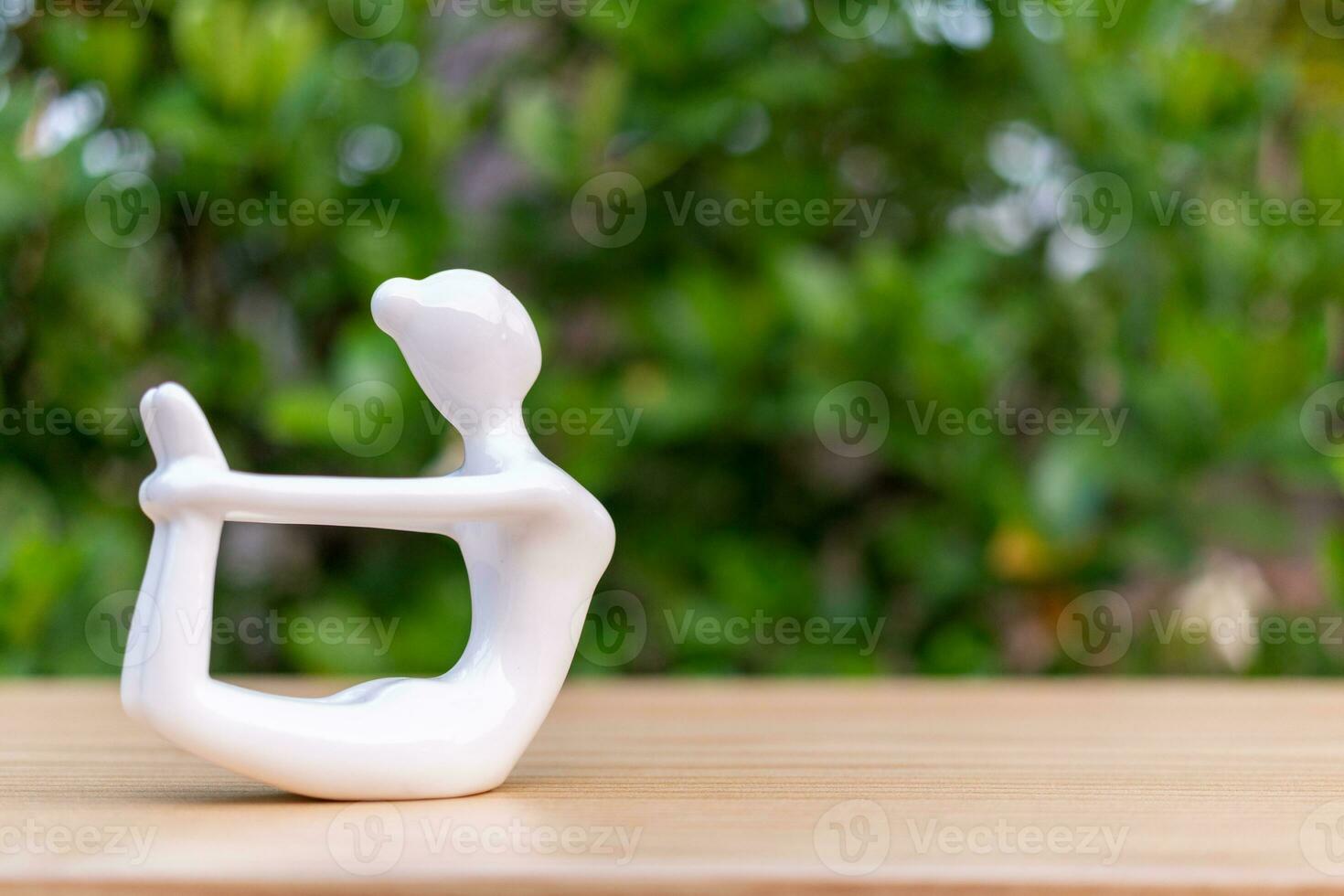 ceramica yoga figurina di donna fare yoga posa su di legno pavimento e verde foglia sfondo foto