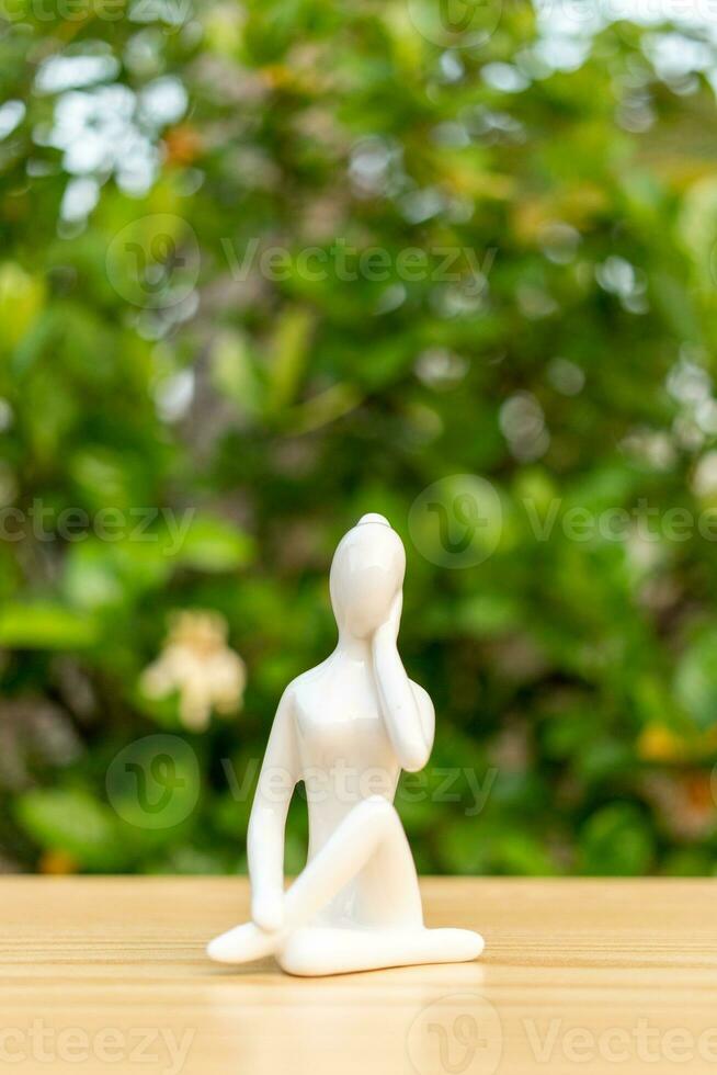 ceramica yoga figurina di donna fare yoga posa su di legno pavimento e verde foglia sfondo foto