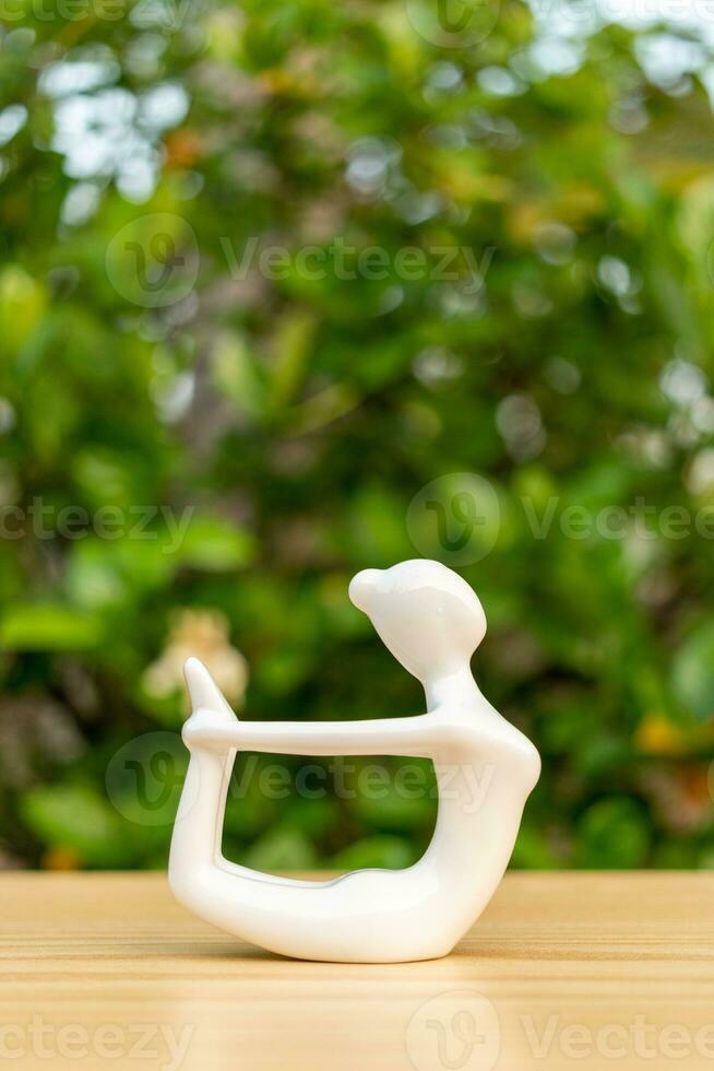 ceramica yoga figurina di donna fare yoga posa su di legno pavimento e verde foglia sfondo foto