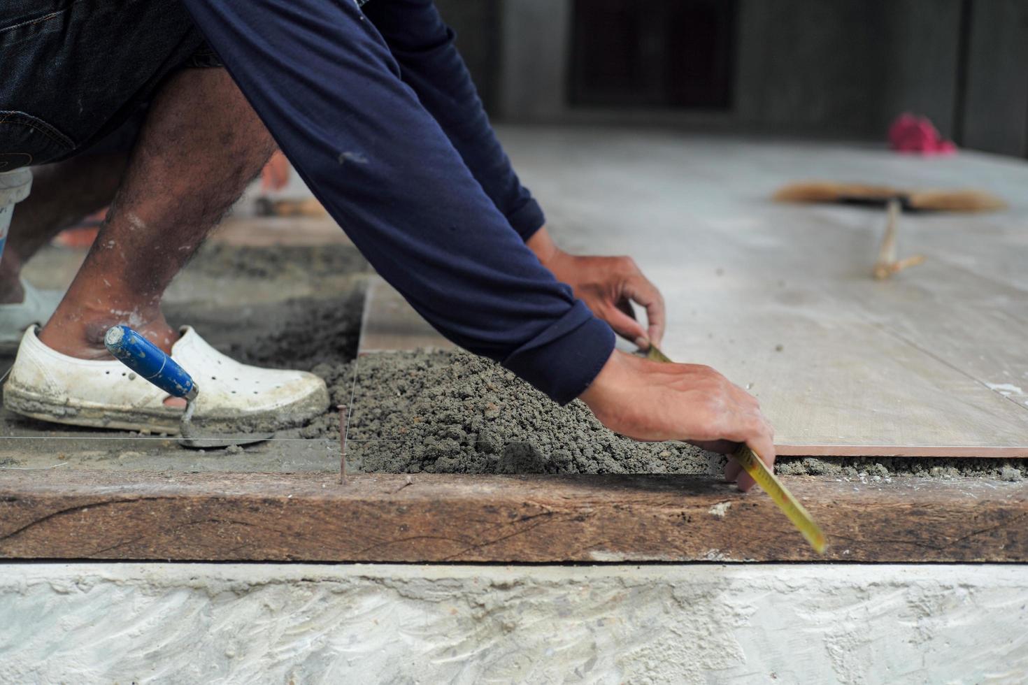 lavoratore che utilizza la spatola di legno durante la posa delle piastrelle del pavimento foto