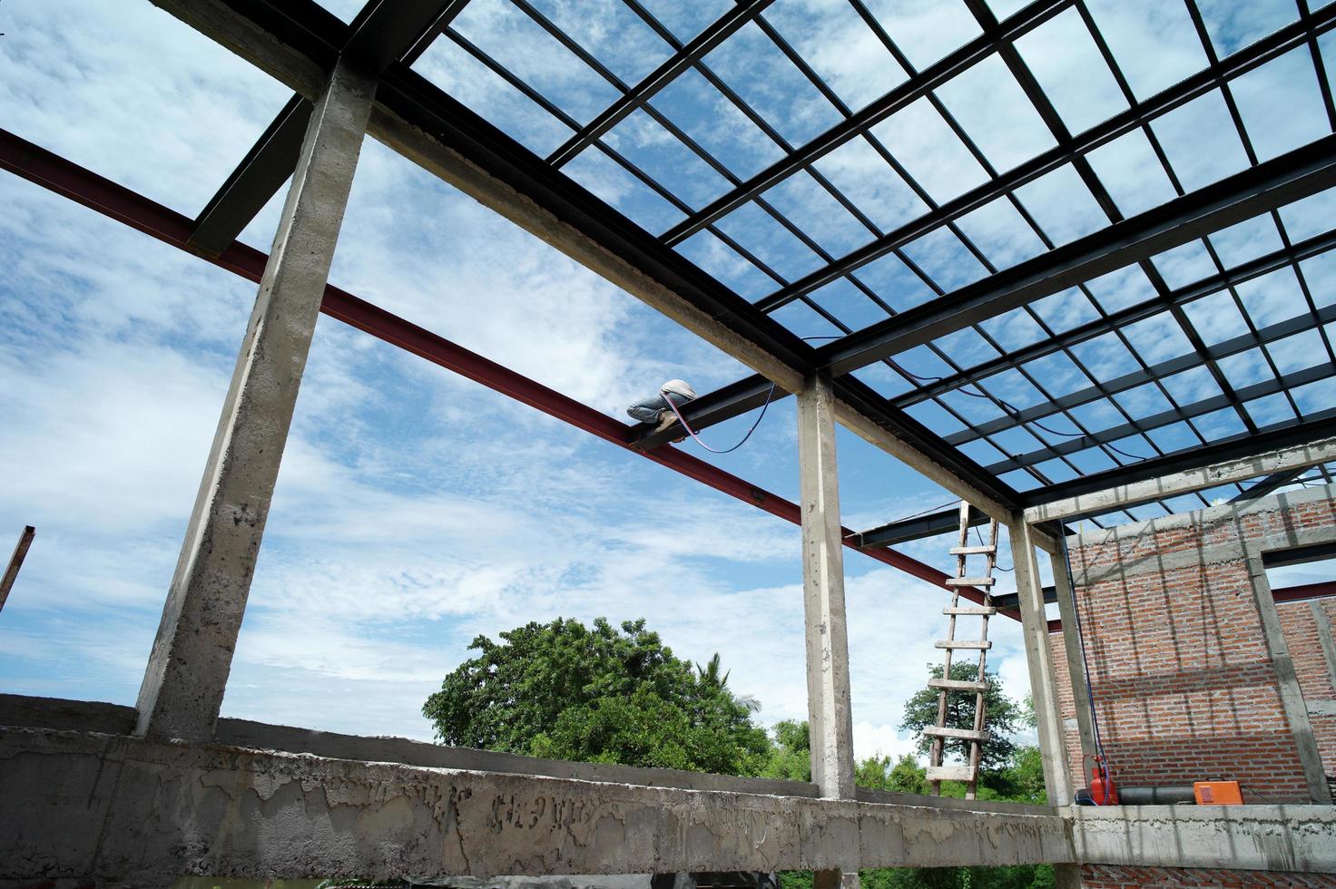 vista posteriore di un saldatore che fa i lavori in acciaio sulla struttura del tetto della casa in costruzione foto