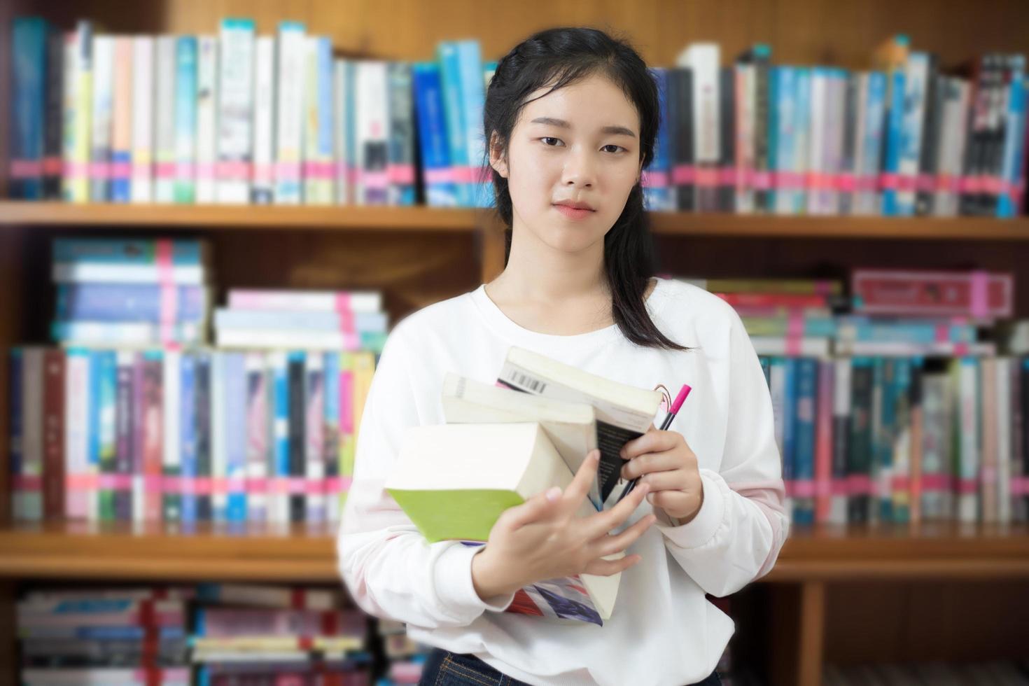 studente asiatico in possesso di libri in biblioteca foto