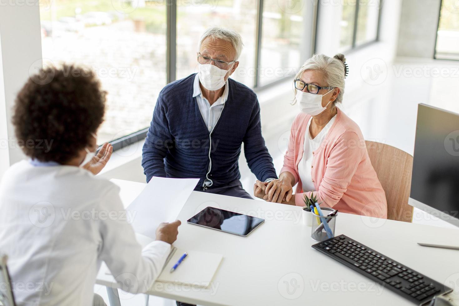 medico che parla alla coppia matura alla scrivania con le maschere foto