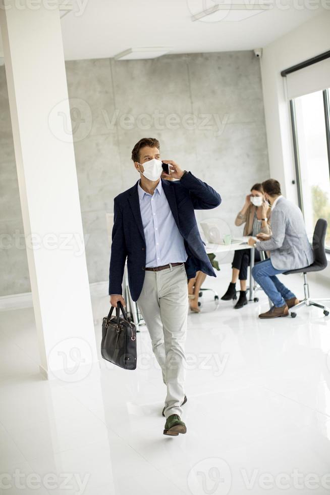 vista verticale di un uomo d'affari mascherato prendendo il telefono e camminare foto