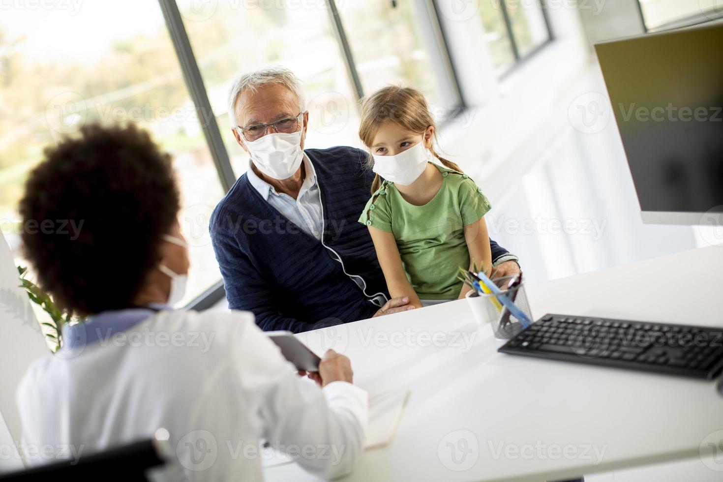 nonno mascherato e nipote a parlare con il medico alla scrivania foto