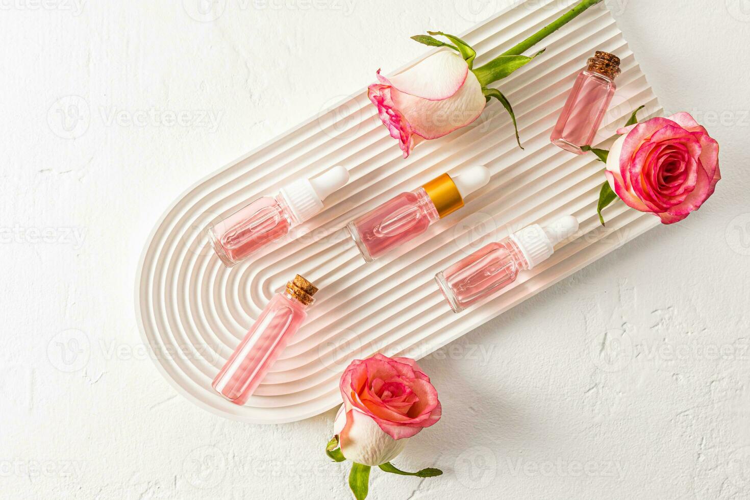 superiore Visualizza di un' bellissimo composizione di cosmetico bottiglie con un' Prodotto di rosa petali e mini cuffie di vivere Rose su un' bianca gesso vassoio arco. piatto posizione. foto