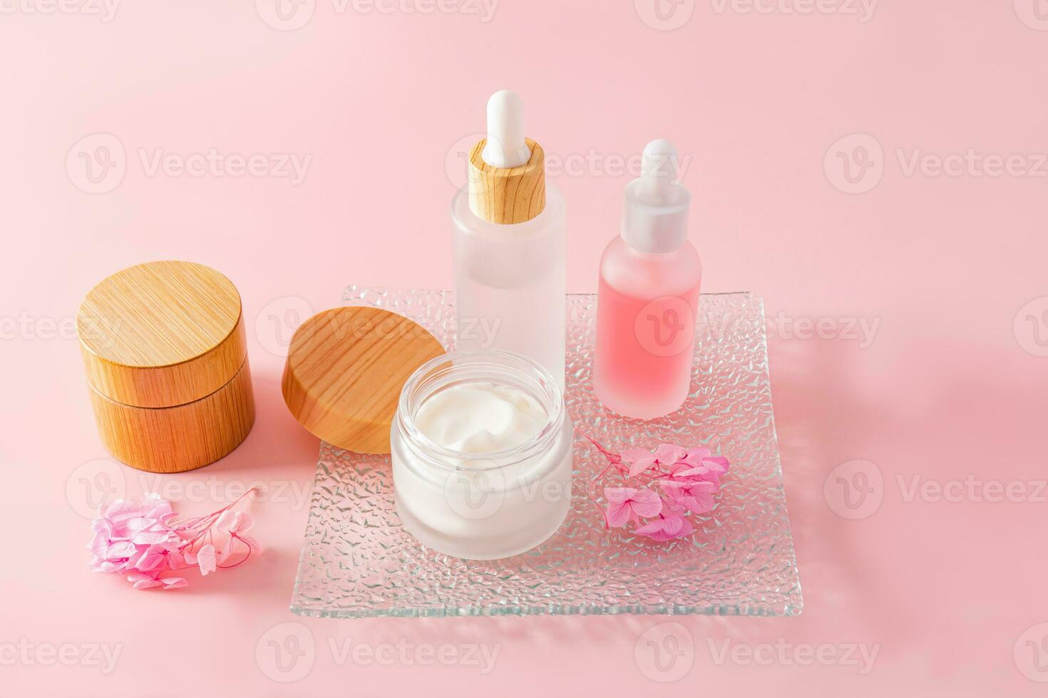 un' alla moda cosmetico Prodotto nel bicchiere Opaco bianca bottiglie e crema nel un' vaso su un' bicchiere sbalzato vassoio e un' rosa sfondo. naturale cosmetici. foto