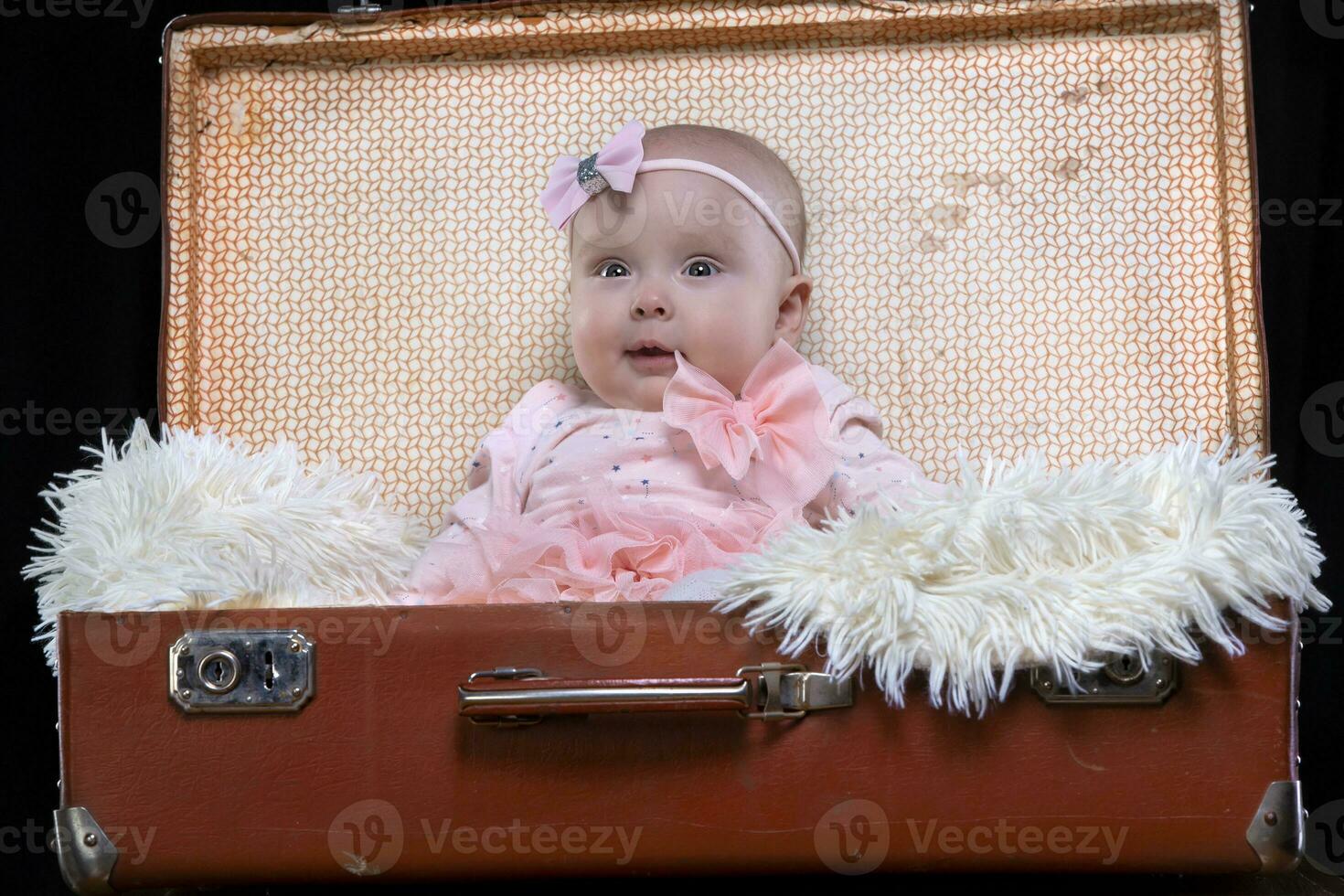 un' poco bambino si siede nel un' retrò valigia e sorrisi. bella bambino. foto