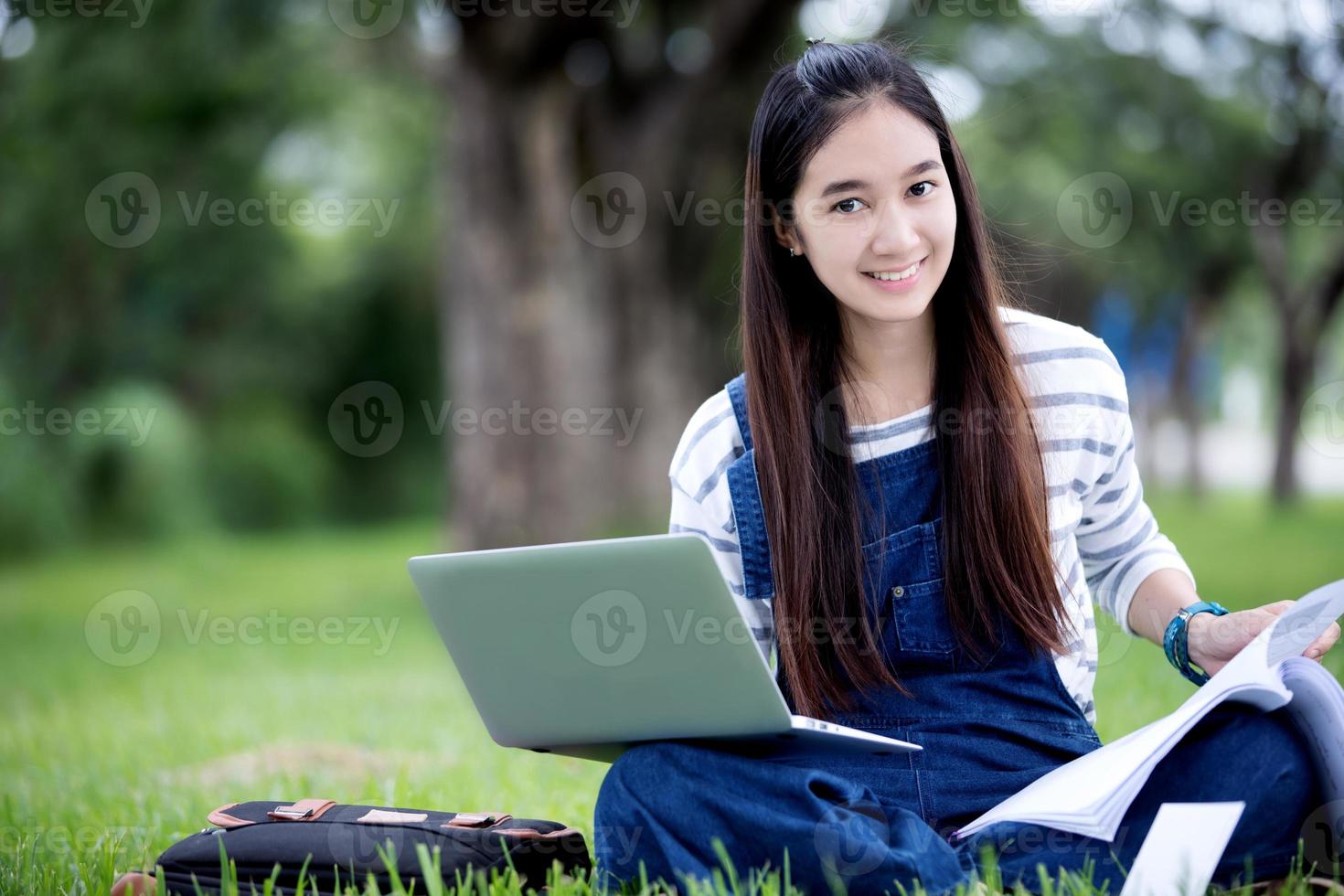sorridente bella ragazza asiatica leggendo il libro e lavorando nel parco foto