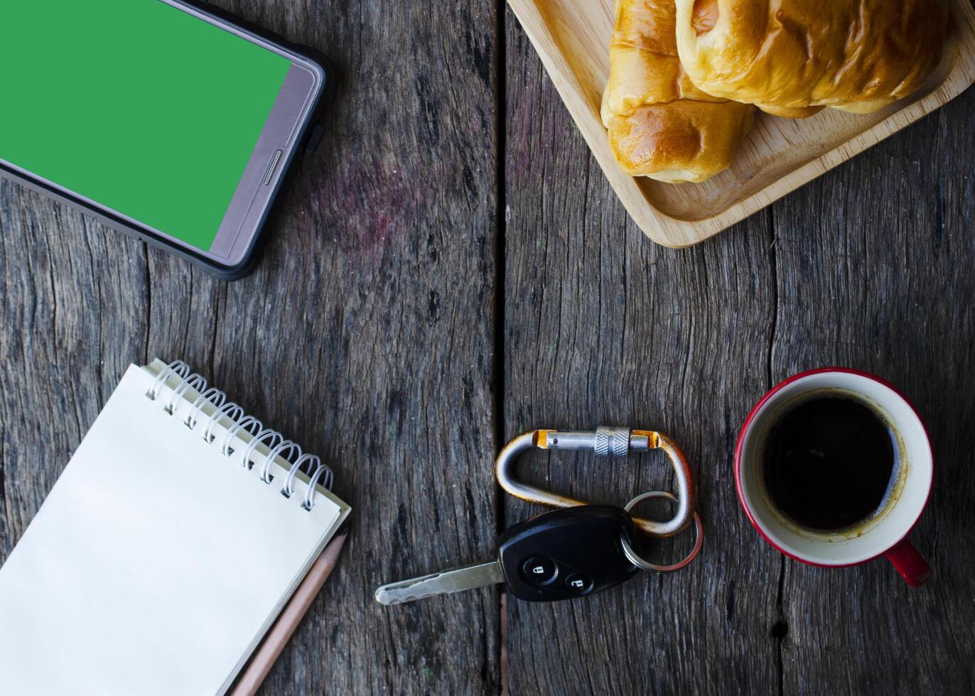 chiave della macchina e tazza di caffè con gustosi panini, telefono cellulare e blocco note sul fondo della tavola in legno foto