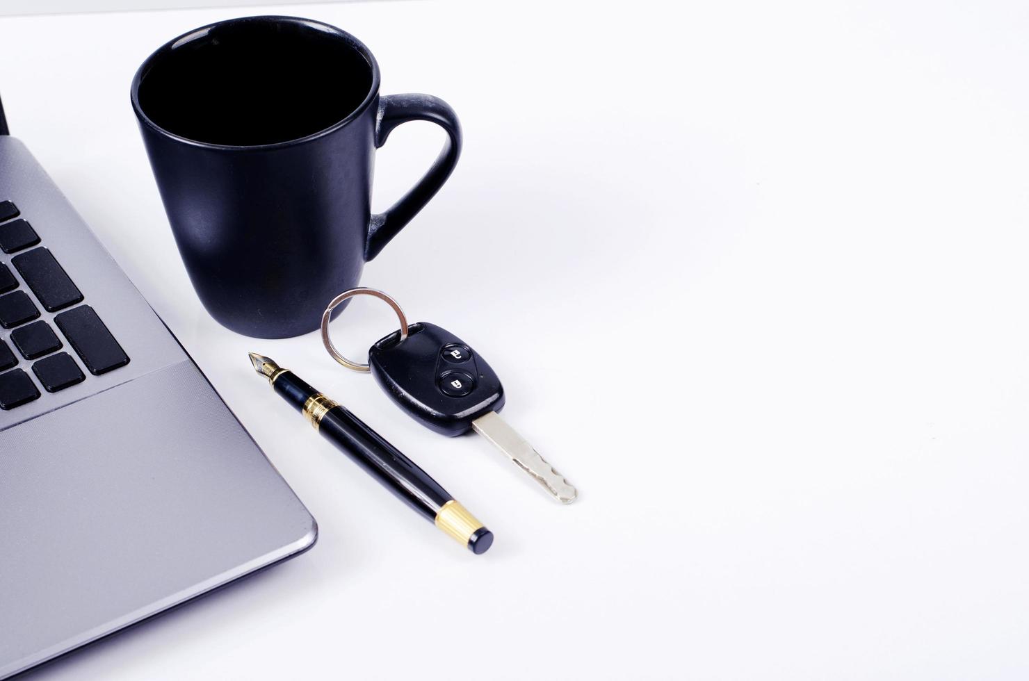 tazza di caffè e penna stilografica e chiave della macchina con il computer portatile su sfondo bianco con copia spazio per il testo foto