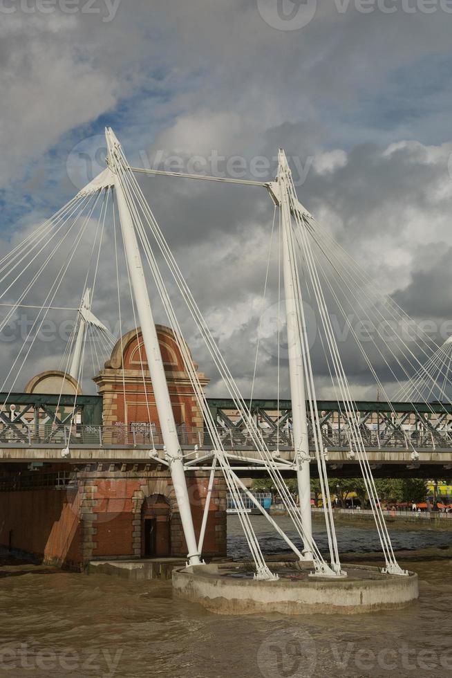 Vista dei ponti del giubileo d'oro e la stazione di Charing Cross dalla riva sud del fiume Tamigi a Londra in una torbida giornata estiva foto