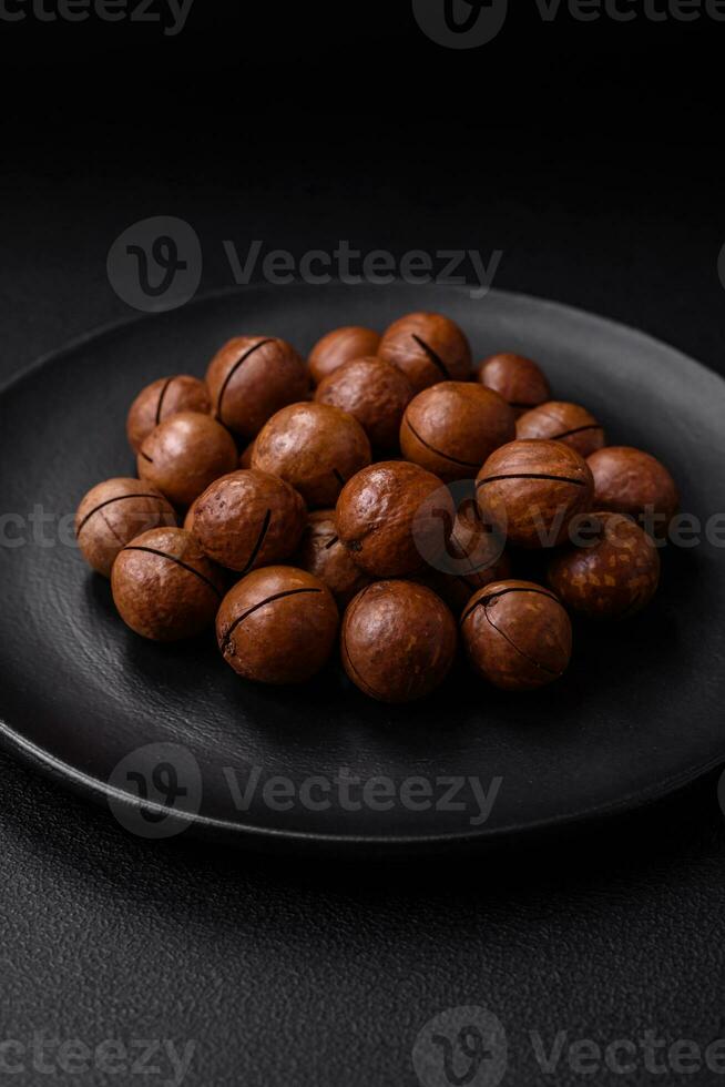 delizioso arrostito macadamia noccioline nel conchiglia su un' buio strutturato sfondo foto