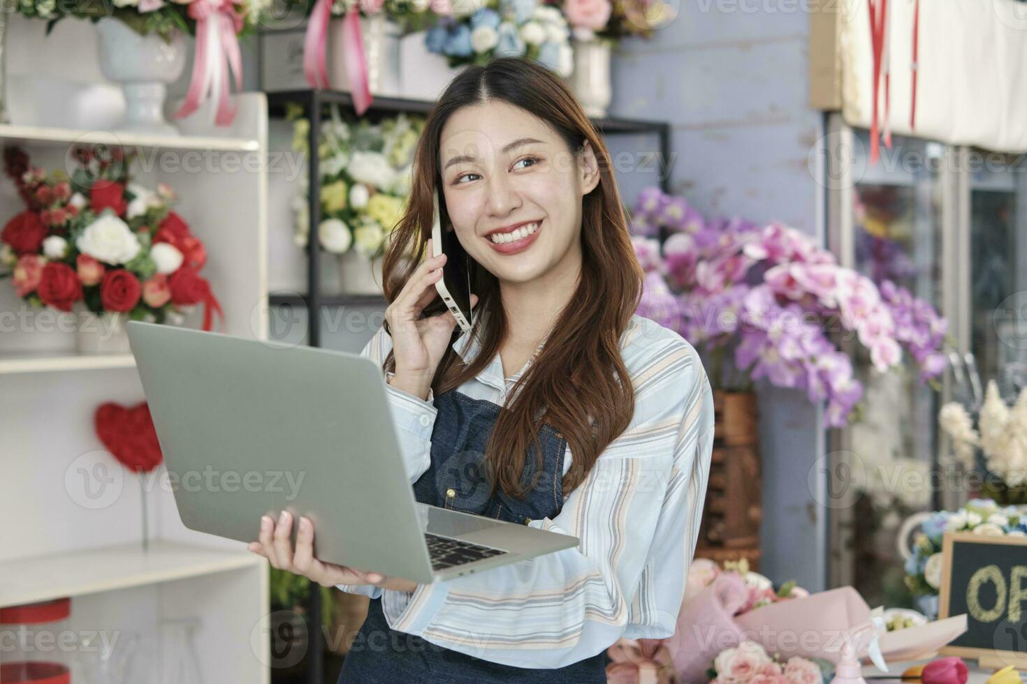 uno giovane asiatico femmina fioraio proprietario, Lavorando con computer portatile, vendita floreale organizzare, parlando su mobile Telefono nel colorato fiore negozio memorizzare con un' bellissimo mazzo di fiori, e e-commerce attività commerciale. foto