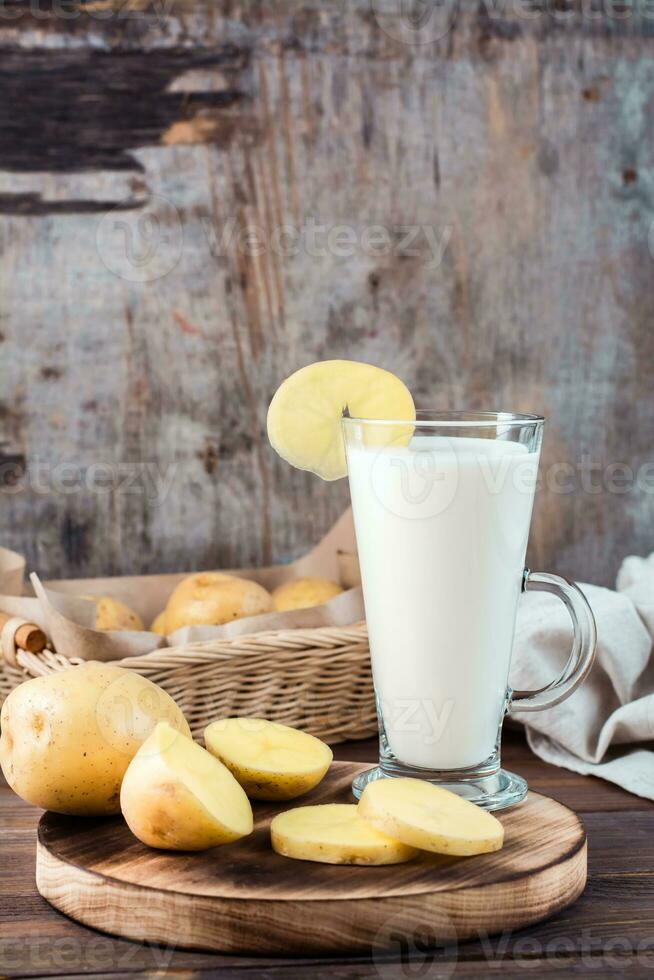 alternativa verdura vegano Patata latte nel un' bicchiere e Patata tuberi lato di lato su un' di legno tavolo. vegetariano cibo. verticale Visualizza. copia spazio foto