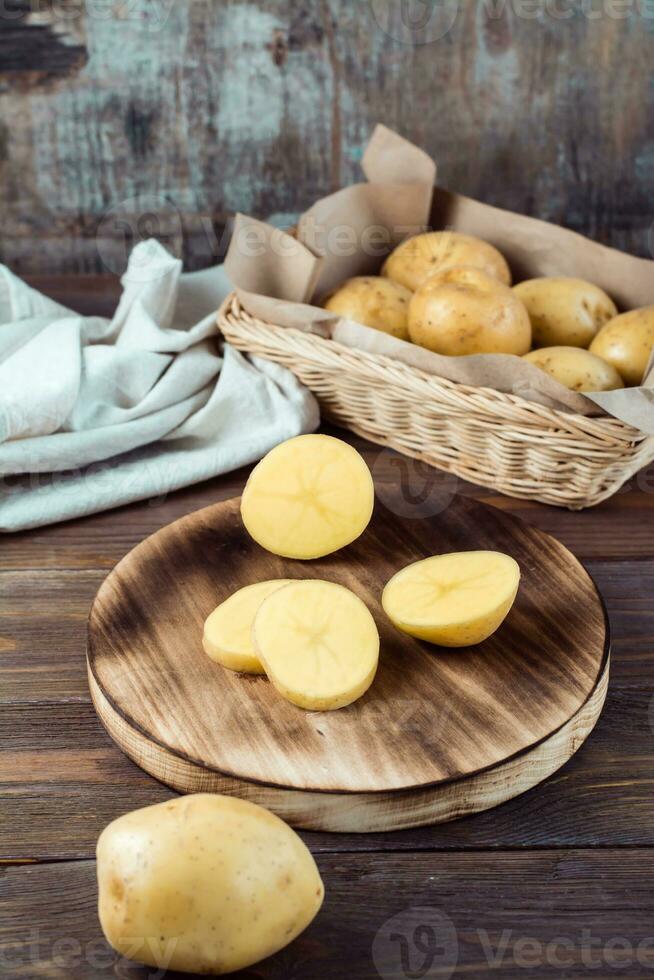 fresco giallo patate tagliare in pezzi su un' tavola e un' cestino con tuberi su un' di legno tavolo. vegetariano cibo. verticale Visualizza foto