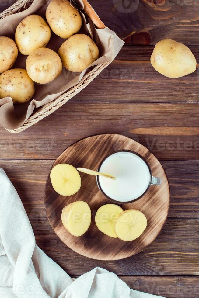 alternativa verdura vegano Patata latte nel un' bicchiere e Patata tuberi lato di lato su un' di legno tavolo. vegetariano cibo. verticale e superiore Visualizza foto