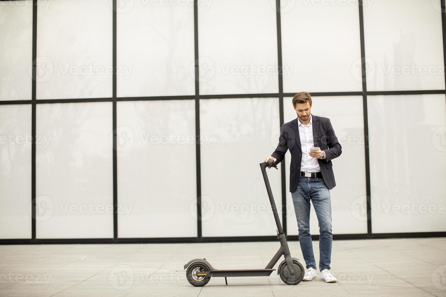 uomo che tiene uno scooter e guardando il telefono foto