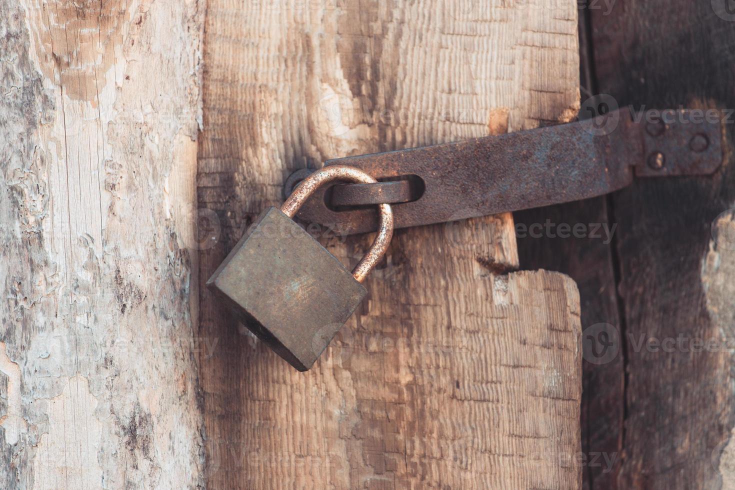 il vecchio e vintage lucchetto in metallo con ruggine sulla porta di legno chiusa per sicurezza foto