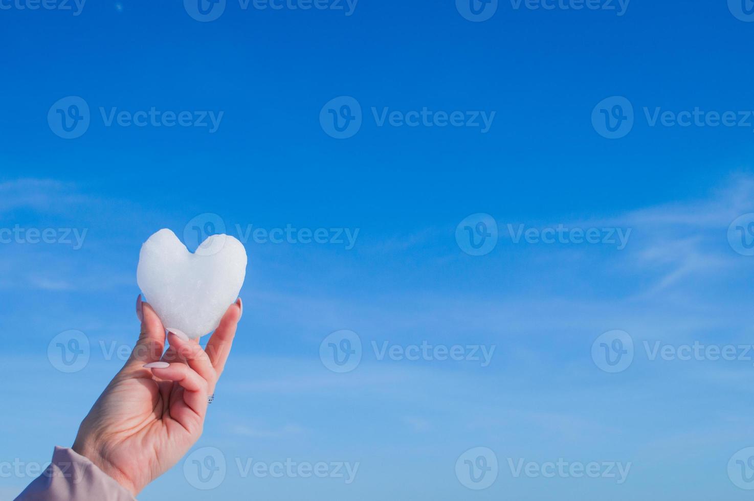 mani femminili con cuore bianco dalla neve nella giornata invernale foto