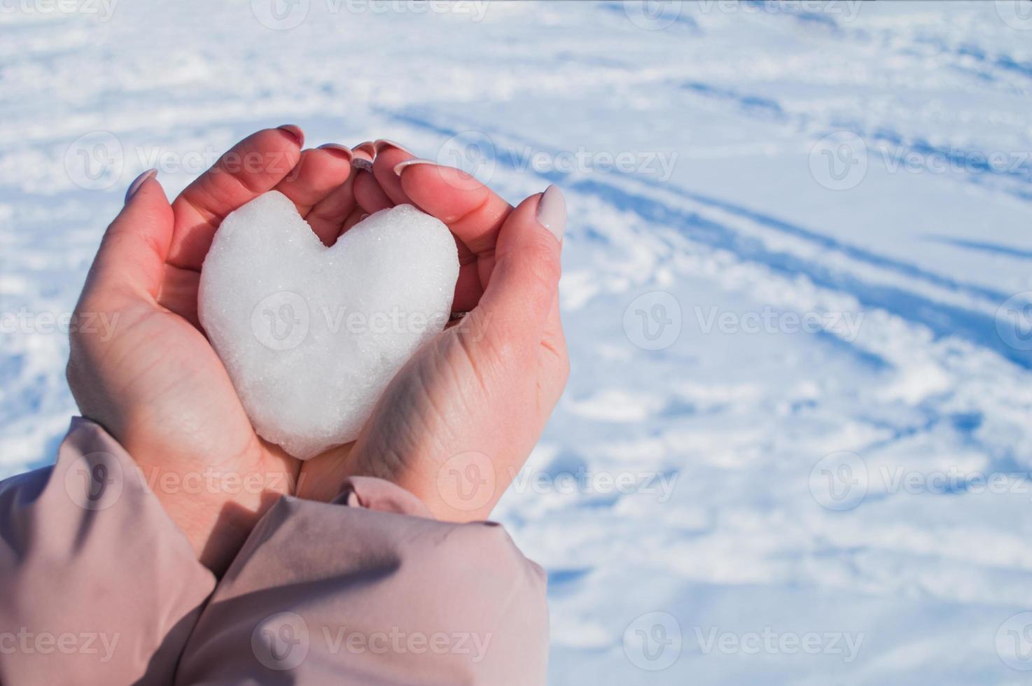 mani femminili con cuore bianco dalla neve nella giornata invernale foto